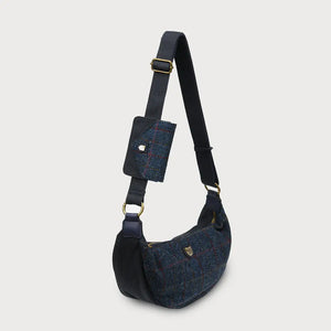 A side view of a navy over-check Harris Tweed Luna bag with a matching purse attached, on a white background.