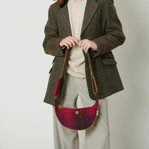 A woman with red hair is holding a red tartan Islander Harris Tweed Luna bag in front of her.