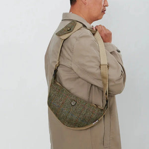 A man, wearing a beige overcoat and jeans, is carrying a chestnut herringbone Islander Harris Tweed Luna bag over his shoulder.