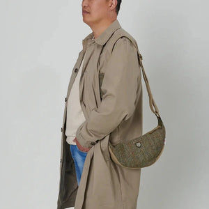 A man, wearing a beige overcoat and jeans, is carrying a chestnut herringbone Islander Harris Tweed Luna bag over his shoulder.