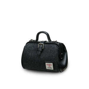 A black herringbone Harris Tweed mini doctor bag tilted at an angle, showcasing its two top handles and compact size. (Islander)