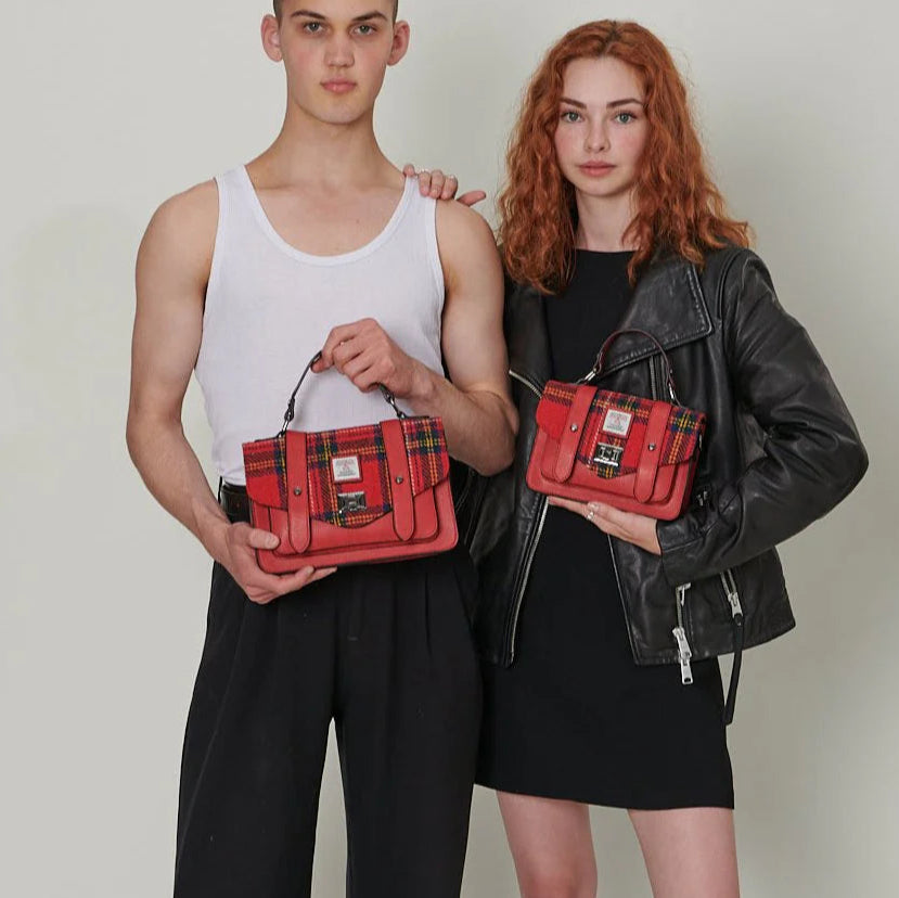 Two models standing side by side holding matching Islander Harris Tweed Satchels in Royal Stewart Tartan – showcasing full and mini sizes in a modern, gender-neutral style.