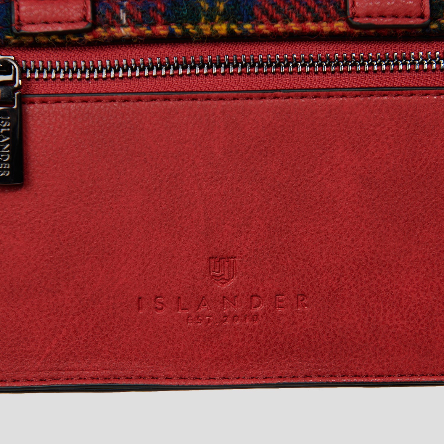 Detailed shot of Islander branding embossed into red vegan leather on back of the satchel.
