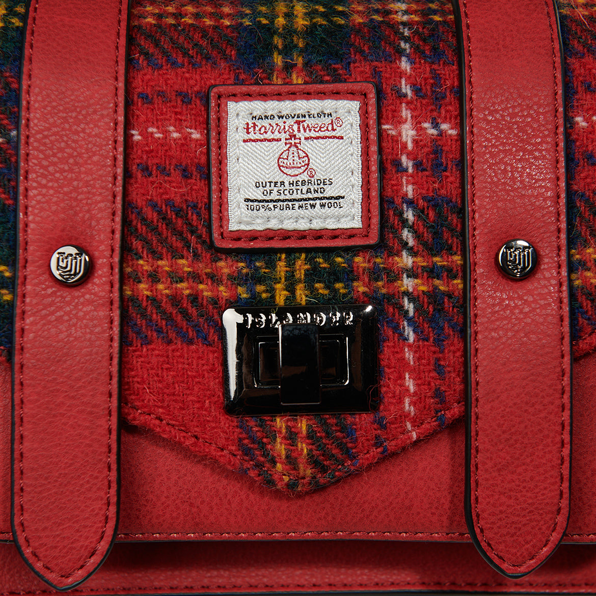 Close-up of Harris Tweed certification patch and silver twist-lock clasp on red tartan satchel.