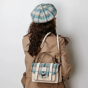 Coastal Charm: A woman with a relaxed smile glances to the side, her hair cascading down her shoulders and contrasting beautifully with an Islander cream and blue tartan lambswool bunnet. 