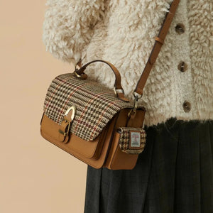 A woman wearing a beige Harris Tweed Melrose Leather Crossbody Bag over her shoulder. The bag is made from genuine leather and features a traditional Harris Tweed pattern.