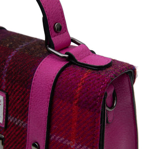 Close up of the top handle of the satchel showing the contrasting pink leather and red tartan fabric.