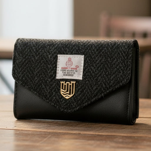Black herringbone Harris Tweed clasp purse on wooden table with leather base.