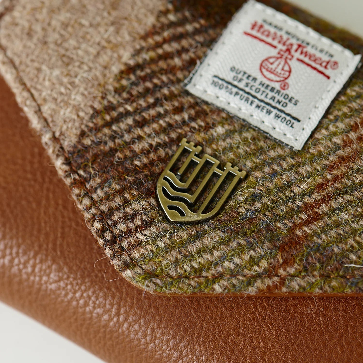 Close-up of gold shield badge and Harris Tweed label on chestnut purse.