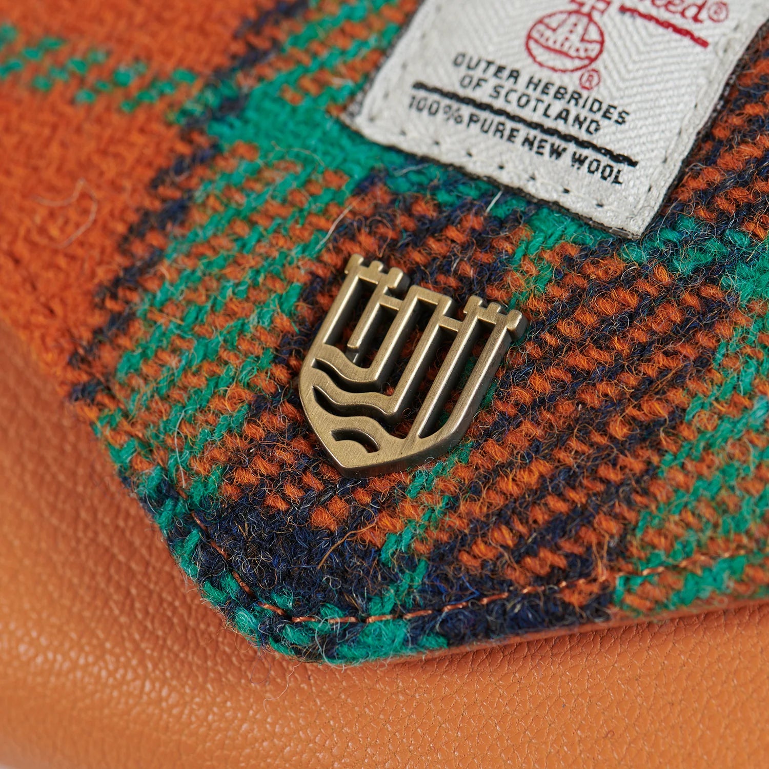 Close-up of Harris Tweed label and gold badge on orange-blue tartan purse.