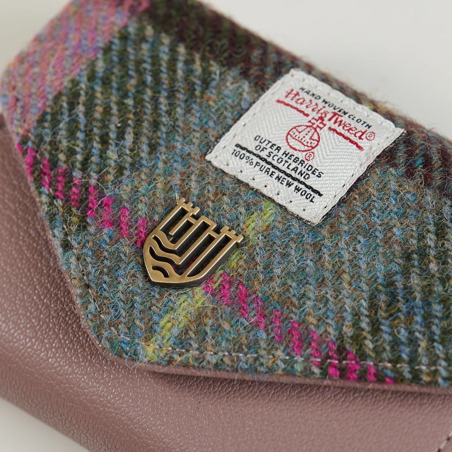 Close-up of Harris Tweed label and tartan weave on pink-green purse.