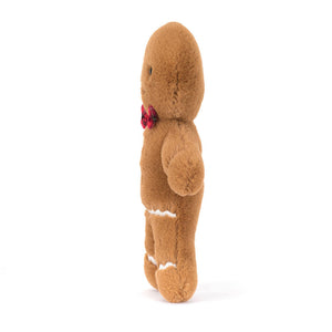 Side: Jolly Gingerbread Fred, a soft and cuddly plush toy from Jellycat, is shown sideways. Fred has a golden brown body with embroidered stitching details that resemble icing and buttons.  He also has a red tartan bowtie.