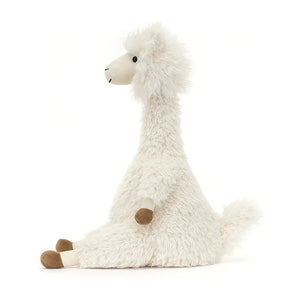 From the side Jellycat Alonson alpaca sits with their legs stretched out in front.