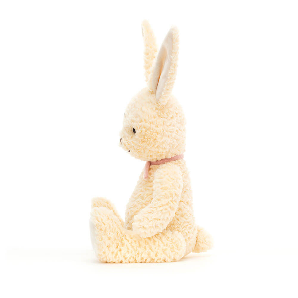 A side view of a soft, white bunny plush toy. It is sitting down with its ears flopping. The toy is made by Jellycat.