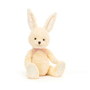 A cuddly, white bunny plush toy sitting upright, smiling with big, round eyes. The toy is made by Jellycat.