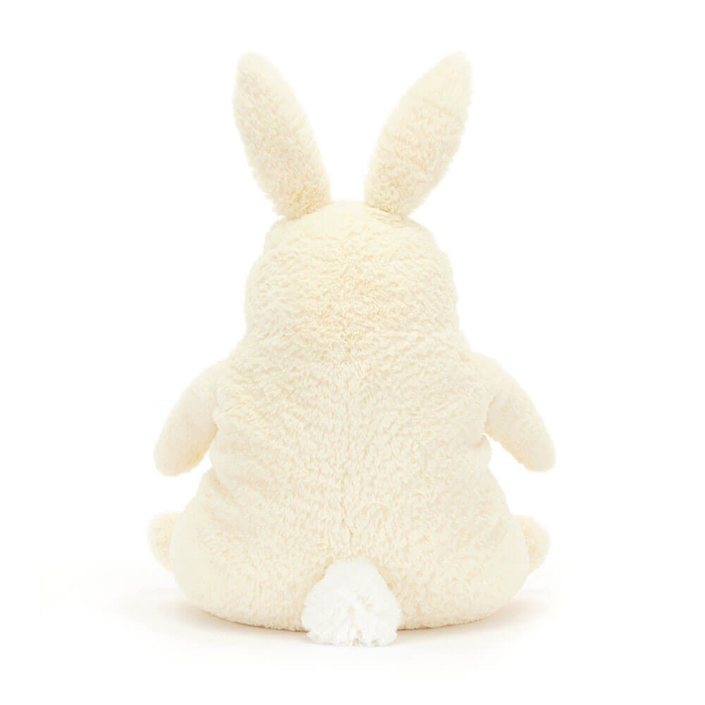 The back of a cream bunny plush toy. The toy is sitting down and has a fluffy tail. The toy is made by Jellycat.