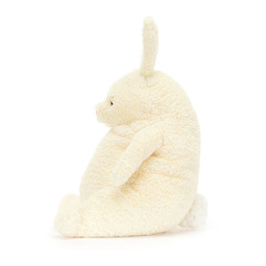 A side view of a soft, cream bunny plush toy. It is sitting down with its ears flopping. The toy is made by Jellycat.