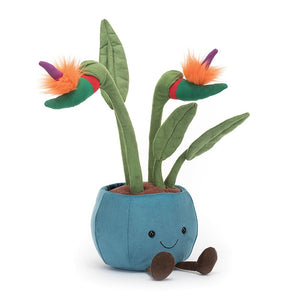 A luxuriously soft Jellycat Amuseable Bird of Paradise plush plant, tilted slightly to reveal its vibrant red, green, and purple flowers with fuzzy orange petals. The plant sits in a teal suedette pot filled with fluffy cocoa soil.