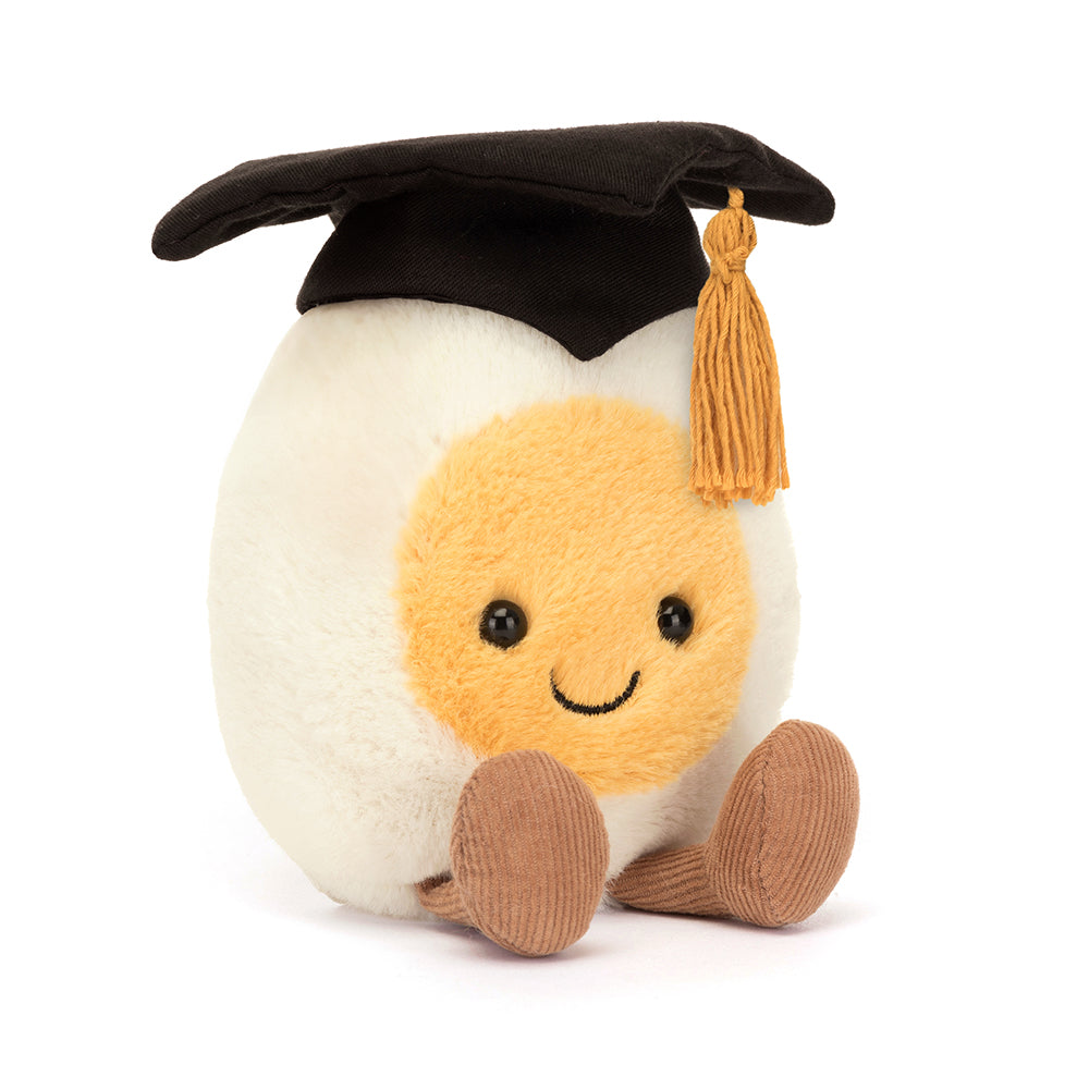 Angled View: Cheeky grin and mortarboard hat! This Jellycat Boiled Egg Graduation Plush is ready to celebrate academic achievements.