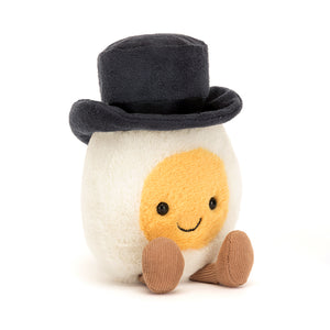 Angled View: Suave Jellycat Amuseable Boiled Egg Groom plush, winking with a charming smile. Sunny yellow yolk, top hat, and bow tie details visible.
