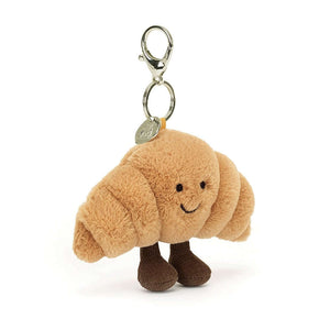 Jellycat bag charm that is in the shape of a croissant. It is soft and fluffy and has little corduroy feet below. 