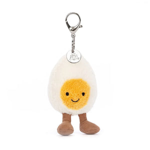 Jellycat Amuseable Happy Boiled Egg Bag Charm, has a silver clip, the egg has soft cream fur and a sunny yellow yolk, brown corded boots and Jellycat Tag.