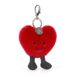 Jellycat Amuseable Heart Bag Charm with plush red fur, embroidered eyes and smile, brown corded boots. It has a silver claw clip and the silver Jellycat tag.