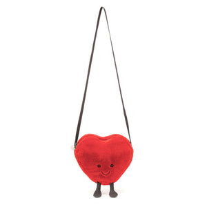 A Jellycat Amuseables Heart Bag hanging from a shoulder strap, showcasing its size and functionality as a bag.