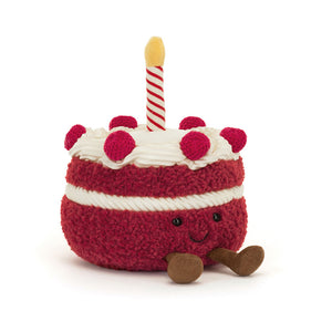 Angled View: Jellycat Amuseables Cheri Cake soft toy, angled view, showing its realistic cake design with buttercream frosting and cherries on top with a striped candle with orange flame.