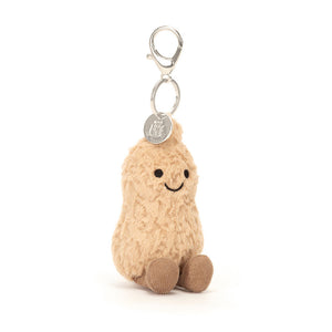 Angled View: Playful peanut on the go! The Jellycat Amuseables Peanut Bag Charm sits tilted, showcasing its quirky textured shell, toffee cord boots, and a friendly stitch grin. A cheeky addition to your bag!