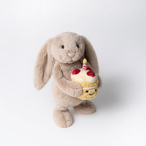 Jellycat Bashful Beige Birthday Bunny standing and holding the cupcake against a white background.