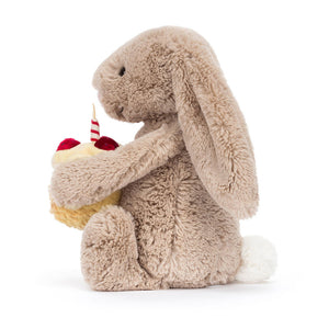 Side view of the Jellycat Birthday Bunny sitting, showing its floppy ears and fluffy tail.