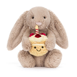 Jellycat Birthday Bunny nibbling on the birthday cupcake plush, with a striped candle on top.