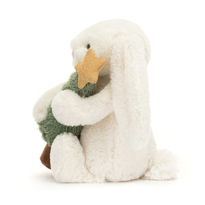 Side: Side view of Jellycat Bashful Bunny plush toy, showing its soft fur and the Christmas tree in its arms.