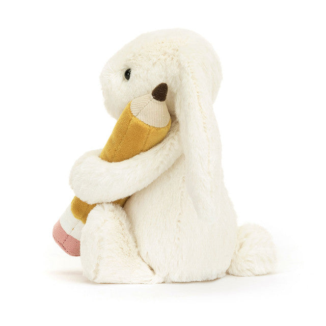 Side View:  Jellycat Bashful Bunny with Pencil: This 18 cm tall bunny companion boasts a soft, huggable design and a unique pencil accessory, ideal for exam season or everyday fun.