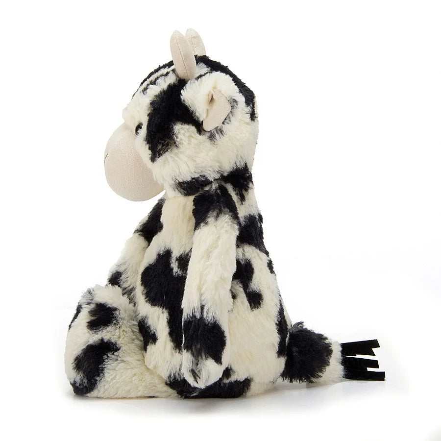 A side view of Jellycat Bashful Calf has creamy white and black patchy fur and two short white horns.