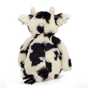 A rear view of Jellycat Bashful Calf has creamy white and black patchy fur and two short white horns. The Tail is fur and suede .