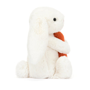 Side View: Jellycat Bashful Carrot Bunny plush white bunny with a fluffy tail holding a carrot.