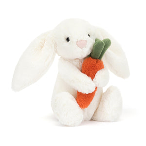 angled View: Jellycat Bashful Carrot Bunny plush white bunny holding a carrot.