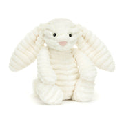 Angled View: Heavenly cuddles! The Jellycat Bashful Luxe Bunny Nimbus leans in, showcasing its luxurious double-cream plush with floppy ears and a silky tail. Glossy eyes and a dainty suedette nose complete the celestial look. Snuggle up to pure softness! 