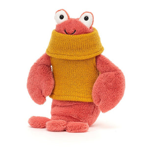 A playful Jellycat Cozy Crew Lobster, tilted at an angle, with soft peachy-pink plush, squidgy segments, and a stylish mustard rollneck jumper.