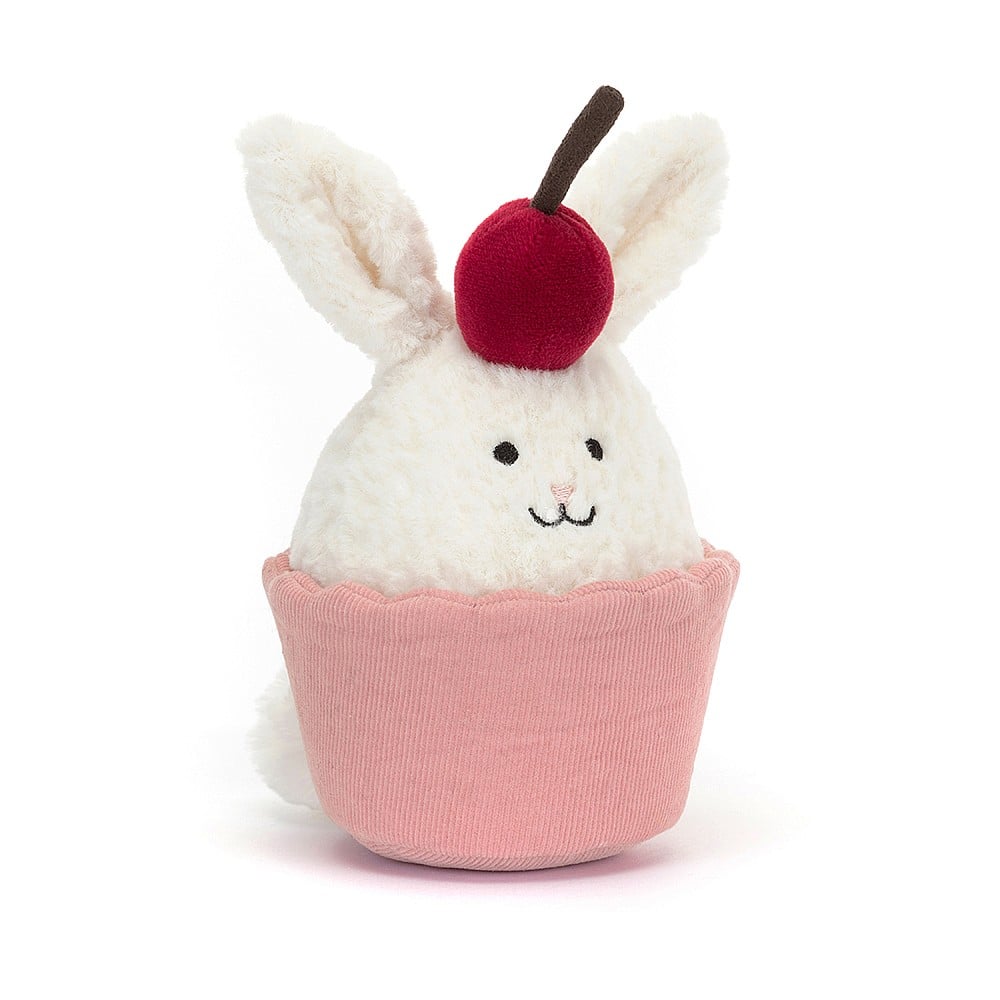 Playful surprise! Fluffy cream bunny peeks out from pink cord "cake," wearing a cherry hat with a mischievous grin. Jellycat Dainty Dessert Bunny Cupcake - cute and cuddly chaos!