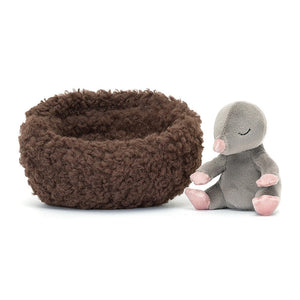 A sleepy-eyed Jellycat Hibernating Mole, with soft grey fur, pink nose, and embroidered closed eyes, rests outside its cozy cocoa bed. Perfect for cuddling adventures!