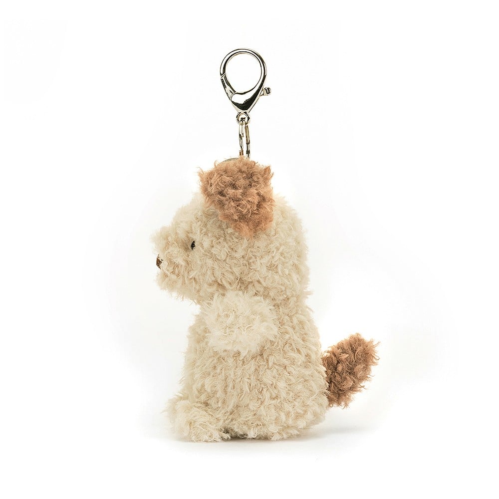 A side view of Jellycat Little Pup Bag Charm. The small, plush puppy has fluffy nougat fur with brown patches. It is attached to a silver clasp.