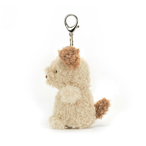 A side view of Jellycat Little Pup Bag Charm. The small, plush puppy has fluffy nougat fur with brown patches. It is attached to a silver clasp.