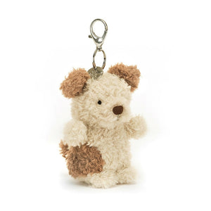 Jellycat Little Pup Bag Charm. The small, plush puppy has fluffy nougat fur with brown patches, perky ears, and a playful grin. It is attached to a silver clasp, ready to be clipped onto a bag or backpack