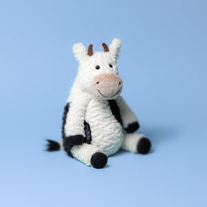 Jellycat Mooliet Cow sitting on a blue background, showcasing its soft and cuddly design.