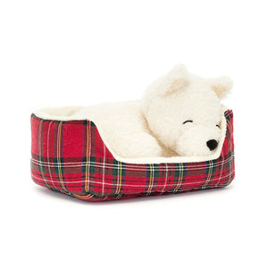 Angled View: Jellycat Napping Nipper Westie resting peacefully at an angle, curled up in a cozy quilted tartan bed. Shortbread fur, closed eyes, and perky ears with tartan lining create a picture of a napping Westie. 