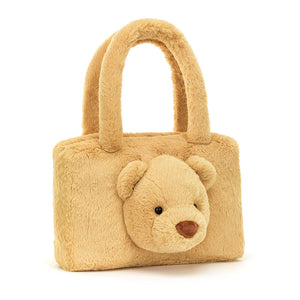 Angled View: Cuddly companion on the go! The Smudge Bear Tote Bag by Jellycat sits tilted, showcasing its soft honeycomb fur, chunky bear face with cute round ears, and secure silver zipper.