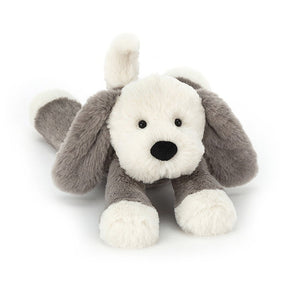 Angled view: Jellycat Smudge Puppy resting with outstretched legs.  This soft pup features floppy ears, a wagging tail, and snowy paws.